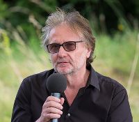 Das Bild zeigt den Autor Mörderndorfer, der eine Sonnenbrille trägt und ein Mikrofon in der Hand hält